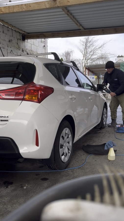 Machine polishing a white Toyota under the canopy at the wash