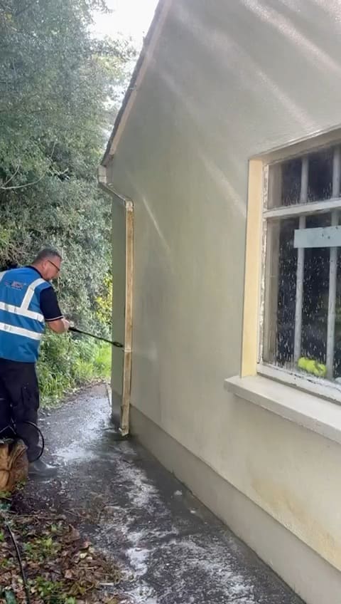 A rendered house wall being washed down with a lance