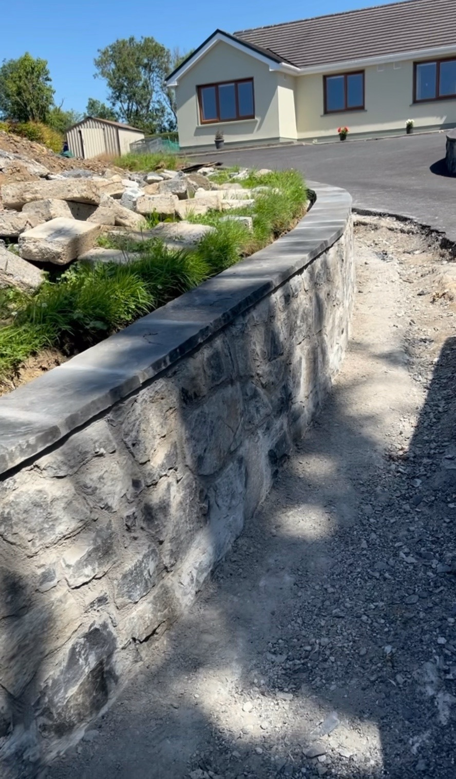 A finished curved stone boundary wall with a level coping, built by Bledar Cankaj